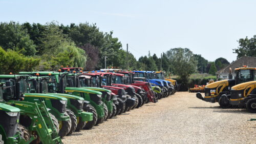 A row of used tractors for sale. Including John Deere, Massey Ferguson, New Holland, Case, Fendt, and Valtra.