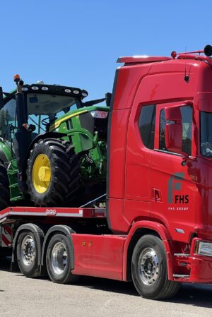 2 Green and yellow John Deere tractors sitting on the bed of a red low loader lorry