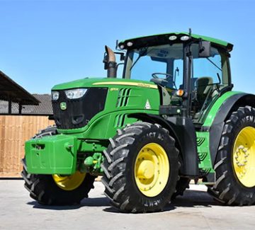 A close-up of a green John Deere tractor with yellow wheels, parked on a paved surface. The tractor has a modern design with a large cab and a prominent exhaust pipe. An example of some of the machines this company sells.